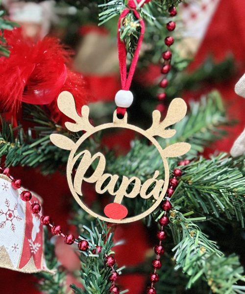 Adorno de madera en forma de reno con la palabra 'Papá' colgado en un árbol de Navidad.