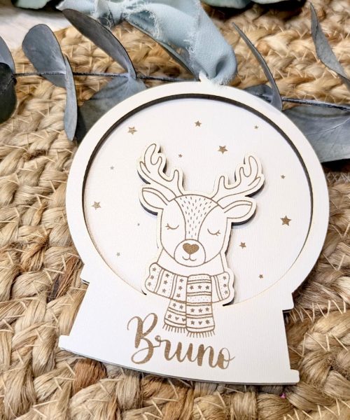 Adorno en forma de bola de nieve con un reno y el nombre Bruno en un diseño de madera clara.